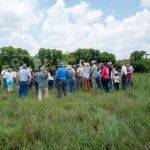 Man speaks to group of people in pasture.